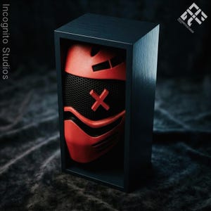 May include: A red and black mask with an X design is displayed inside a dark blue wooden box. The mask has a mesh front and is set against a dark, textured background. The box is rectangular and has a minimalist design.