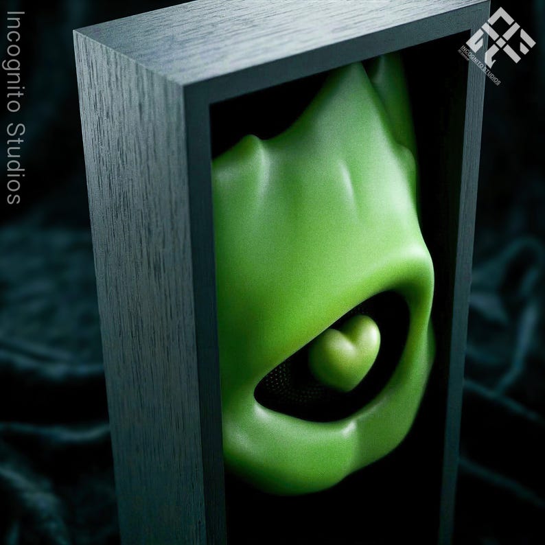 May include: A green, organic-shaped sculpture with a heart-shaped detail, encased in a dark wooden frame. The sculpture has a smooth, glossy finish and is set against a black background. The text "Incognito Studios" is visible.