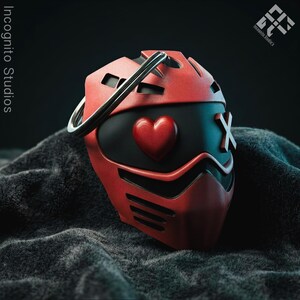 May include: A red and black mask with a heart and an X design. The mask has a silver ring on top and is set against a dark, textured background. The words "Incognito Studios" are visible.