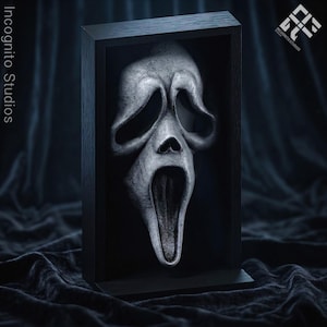 Puede incluir: Escultura enmarcada de una máscara de Scream en escala de grises. La máscara tiene una boca abierta y cuencas de ojos huecas, sobre un fondo negro dentro de un marco de madera negro. El logotipo de Incognito Studios es visible.