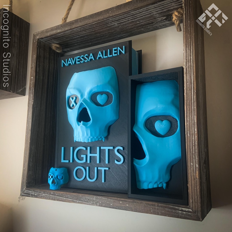 May include: A wooden framed art piece featuring a teal skull design. The artwork includes the text "NAVESSA ALLEN" and "LIGHTS OUT". The skull has heart-shaped eye sockets and an X in one eye socket.