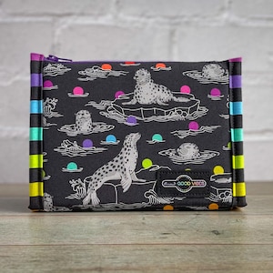 May include: A black zipped pouch featuring a pattern of seals, ice floes, and colourful dots. The pouch has a rainbow-striped border and a small patch that reads "Great Good Vibes".