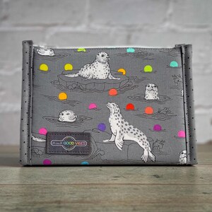 May include: Grey fabric pouch with a sealife pattern. The design features seals, ice floes, and colourful dots. A small label reads "Good Vibes". The pouch has a rectangular shape with rounded corners.