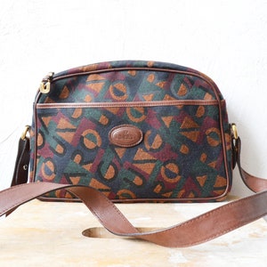 Könnte beinhalten: Eine braune Lederschultertasche mit geometrischem Musterstoff. Die Tasche hat eine goldene Schnalle und einen braunen Lederriemen.