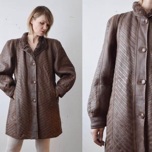 May include: Brown leather coat with a textured, diagonal stripe pattern. The coat has a faux fur collar, button closure, and pockets. The long sleeves extend to the wrists. The coat is knee-length.