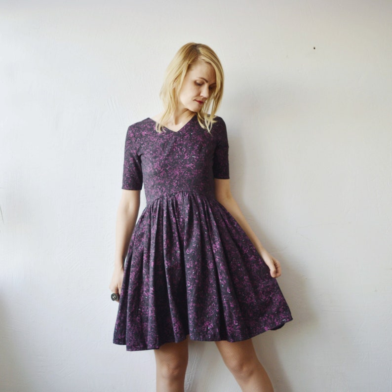 May include: A purple and black floral print dress with a v-neck and short sleeves. The dress has a full skirt and is fitted at the waist.