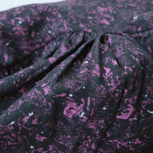 May include: Close-up of a black fabric with a purple and white speckled pattern. The fabric is gathered and has a soft, textured feel.