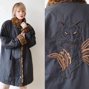Könnte beinhalten: Eine schwarze gesteppte Jacke mit braunem Kunstfellkragen und -ärmelaufschlägen. Die Jacke hat ein gesticktes schwarzes Panther-Design auf der Rückseite.
