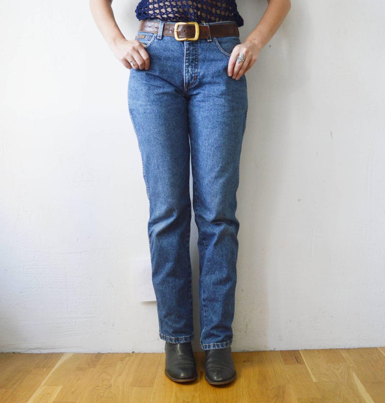 May include: A pair of blue denim jeans with a brown leather belt. The jeans have a straight leg and a high waist.