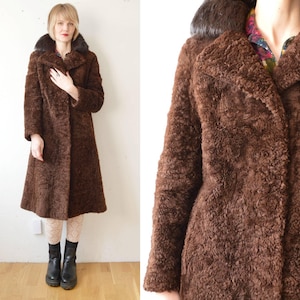 May include: A long brown faux fur coat with a large collar. The collar is made of a darker brown fur. The coat has a button closure.