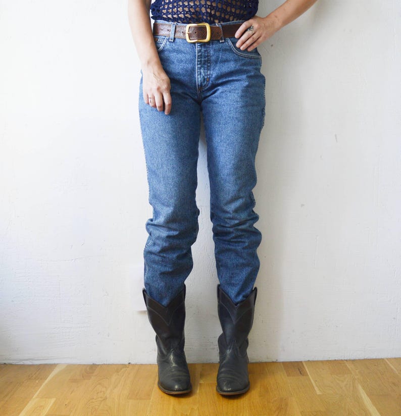 May include: A pair of blue denim jeans with a brown leather belt and black cowboy boots.