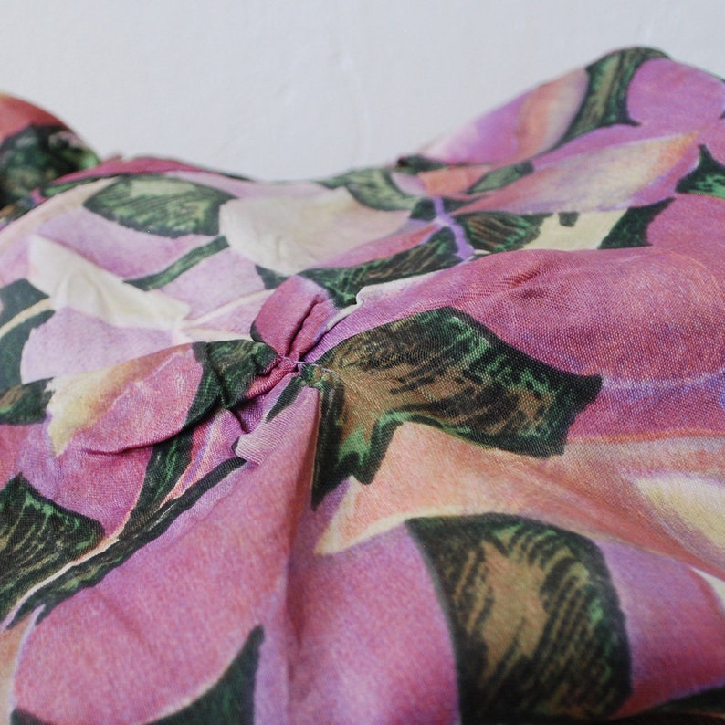 May include: Close-up of a pink and green floral fabric with a gathered section in the center.
