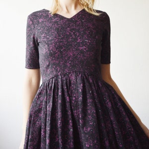 May include: A purple and black patterned dress with a v-neck and short sleeves. The dress has a gathered skirt.