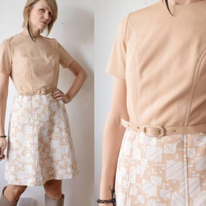 Puede incluir: Vestido beige vintage con mangas cortas y corpiño entallado. El vestido presenta una falda con estampado geométrico y un cinturón a juego. El vestido mide aproximadamente 91 cm de largo.