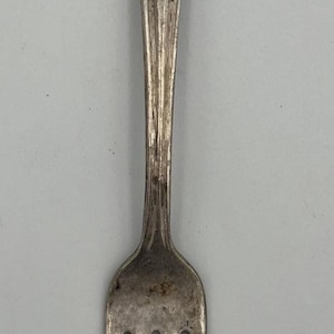 Puede incluir: Tenedor de plata con un diseño floral decorativo en el mango. El tenedor tiene cuatro púas y un aspecto ligeramente deslustrado, lo que sugiere edad o uso. Un utensilio de mesa clásico.