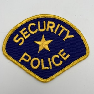 May include: Embroidered patch with a navy blue background and gold trim. The patch features the words "SECURITY POLICE" in gold lettering, with a gold star in the center. The patch has a unique, fan-like shape.