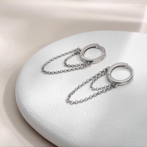 May include: A pair of silver hoop earrings with dangling chains. The chains are made of small, round links.