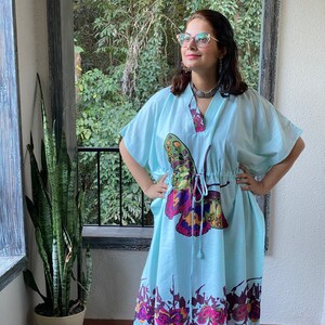 Puede incluir: Una kaftán azul claro con estampado de mariposa y cintura con cordón. La kaftán tiene cuello en V y mangas cortas. El estampado de mariposa es en tonos de rosa, morado, verde y amarillo.