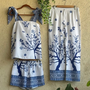 Op de afbeelding: Een witte pyjamaset met een blauwe bloemenprint. De set bevat een tanktop met strikbandjes, een short en een broek.