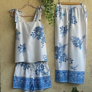 Op de afbeelding: Een witte pyjamaset met een blauw bloemenpatroon. Het topje heeft dunne bandjes die aan de schouders vastgebonden worden. De shorts hebben een elastische tailleband met een trekkoord. De broek heeft een elastische tailleband.