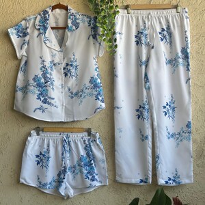 Op de afbeelding: Witte pyjamaset met een blauwe bloemenprint. De set bevat een shirt met korte mouwen, een lange broek en een short.