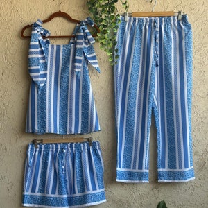 Op de afbeelding: Een blauwe en witte gestreepte pyjamaset met een top, shorts en broek. De top heeft een vierkante halslijn en strikbandjes. De shorts en broek hebben een elastische tailleband.