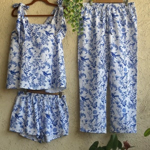 Op de afbeelding: Een witte pyjamaset met een blauwe bloemenprint met vogels. De set bevat een tanktop met strikbandjes, een short en een broek.