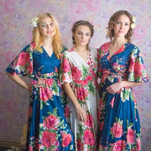 May include: Three women wearing floral print maxi dresses. The dresses have a wrap style and are in shades of blue, white, and pink.