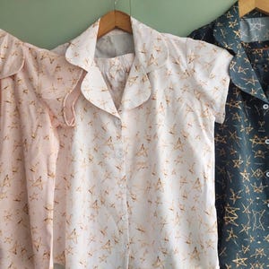 May include: Three button-up shirts with a star print. The shirts are in pink, white, and dark blue.