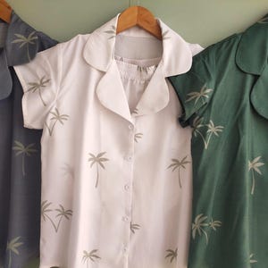 May include: Three short-sleeved shirts with a palm tree print. The shirts are in different colors: dark blue, white, and green.