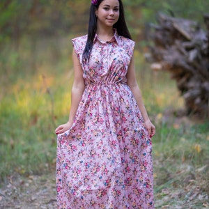May include: A woman wearing a pink floral dress with a purple flower in her hair. She is standing in a forest setting.