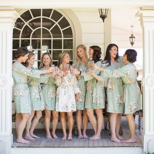 May include: A group of eight women wearing matching floral print robes and holding champagne flutes, smiling and laughing on a porch.