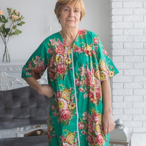 May include: A woman wearing a green floral print dress with a zipper down the front. The dress has short sleeves and a V-neck.
