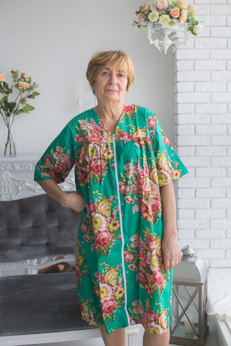 May include: A woman wearing a green floral print dress with a zipper down the front. The dress has short sleeves and a V-neck.