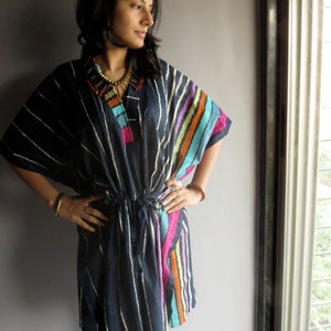 May include: A woman wearing a navy blue and white striped tunic with colorful stripes on the side. The tunic has a drawstring waist and a tassel detail on the neckline.