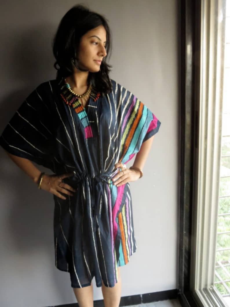 May include: A woman wearing a navy blue and white striped tunic with colorful stripes on the side. The tunic has a drawstring waist and a tassel detail on the neckline.