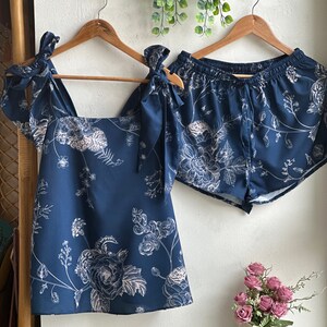 Op de afbeelding: Een blauwe en witte pyjamaset met bloemenprint, bestaande uit een tanktop en een short. De top heeft een vierkante halslijn en de short heeft een elastische tailleband.
