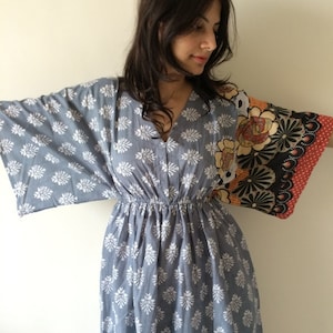 May include: A blue and white floral print dress with a gathered waist and long sleeves. One sleeve features a colorful patchwork design with floral and geometric patterns.