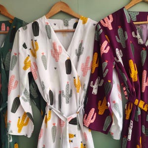 May include: Three long-sleeved robes with a cactus print. The robes are in green, white, and purple.