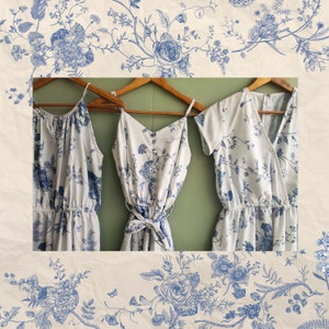 Op de afbeelding: Drie witte jurken met een blauw bloemenpatroon hangen aan houten hangers. De jurken hebben verschillende halslijnen en bandjes. De jurken zijn op een groene achtergrond.