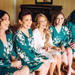 May include: A group of women wearing green floral robes with white trim. The women are smiling and sitting on a couch. One woman is wearing a white robe and has long blonde hair.