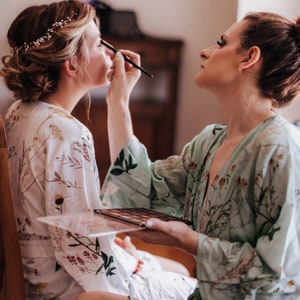 May include: A person applying makeup to another person's eye with a brush. The person applying makeup is holding a makeup palette. Both people are wearing floral print robes.