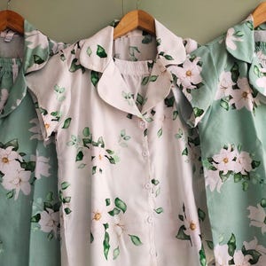 May include: Three floral print pajamas in green and white. The pajamas have a button-up top and a matching bottom. The floral print features white flowers on a green background.