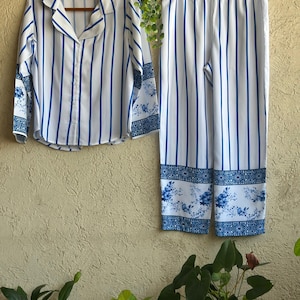 Op de afbeelding: Een gestreepte pyjama in wit en blauw met een bloemenprint op de onderkant van de broek.