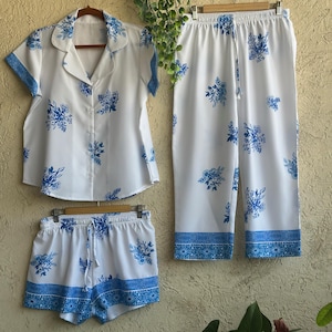 Op de afbeelding: Witte pyjamaset met een blauwe bloemenprint. De set bevat een shirt met korte mouwen, een short en een broek.