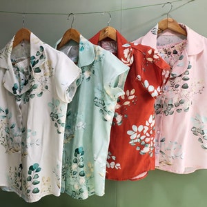 May include: Four short-sleeved shirts with a floral print. The shirts are hanging on hangers and are in different colors: white, light blue, orange, and pink.