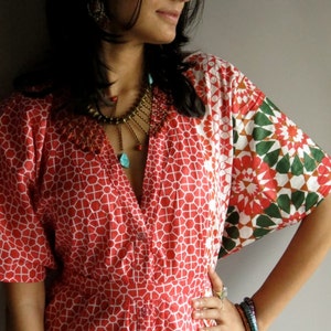 Puede incluir: Una mujer lleva un vestido de estampado geométrico rojo y blanco con un estampado floral verde y blanco en la manga. Lleva un collar de oro con detalles turquesa y varias pulseras en la muñeca.