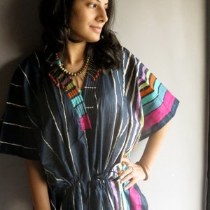 May include: A navy blue and white striped tunic with colorful stripes on the sleeves. The tunic has a drawstring waist and a beaded necklace.