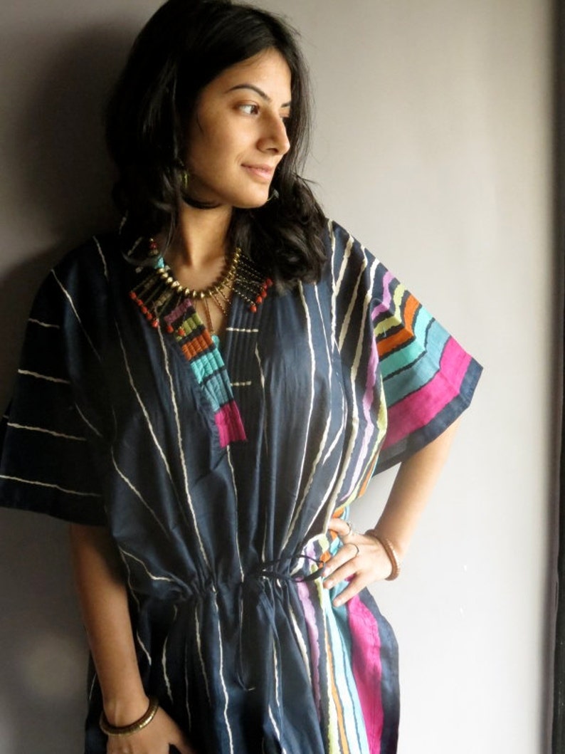 May include: A navy blue and white striped tunic with colorful stripes on the sleeves. The tunic has a drawstring waist and a beaded necklace.