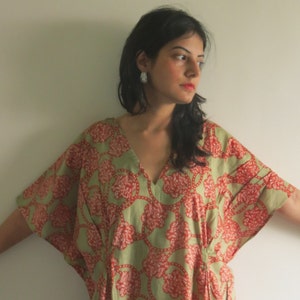 Op de afbeelding: Een vrouw draagt een groene en rode kaftan met een bloemenprint en een V-hals. De kaftan heeft een losse pasvorm en is gemaakt van een zachte, vloeiende stof.